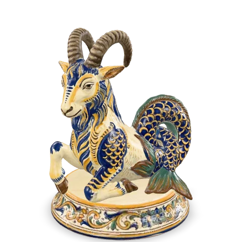 Capra marina in maiolica: davanti una capra con le corna ricurve, dietro una coda di pesce arrotolata a scaglie blu, su una base tonda dipinta.