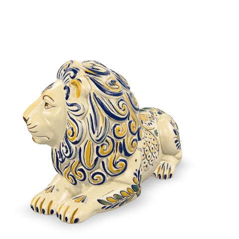 Leone in maiolica sdraiato, il muso calmo e la grande criniera stilizzata a riccioli dipinti in cobalto e zafferano su smalto bianco.