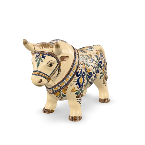 Toro in maiolica in piedi, tozzo e fermo sulle quattro zampe, corna corte, il corpo bianco dipinto con decori popolari blu cobalto e zafferano.