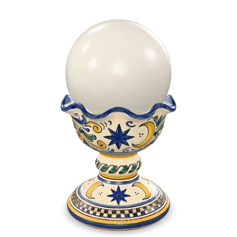 Sfera di cristallo lattiginosa posata su un calice di maiolica dal bordo ondulato, dipinto a mano con stelle e falci di luna in cobalto e zafferano.